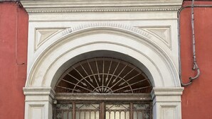 Un'ampia e decorata cancellata in metallo con disegni elaborati, inserita in un arco architettonico classico, affiancata da un muro rosso.