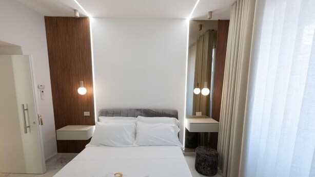 Una camera d'albergo con un letto, comodini, uno specchio, tende e una porta.