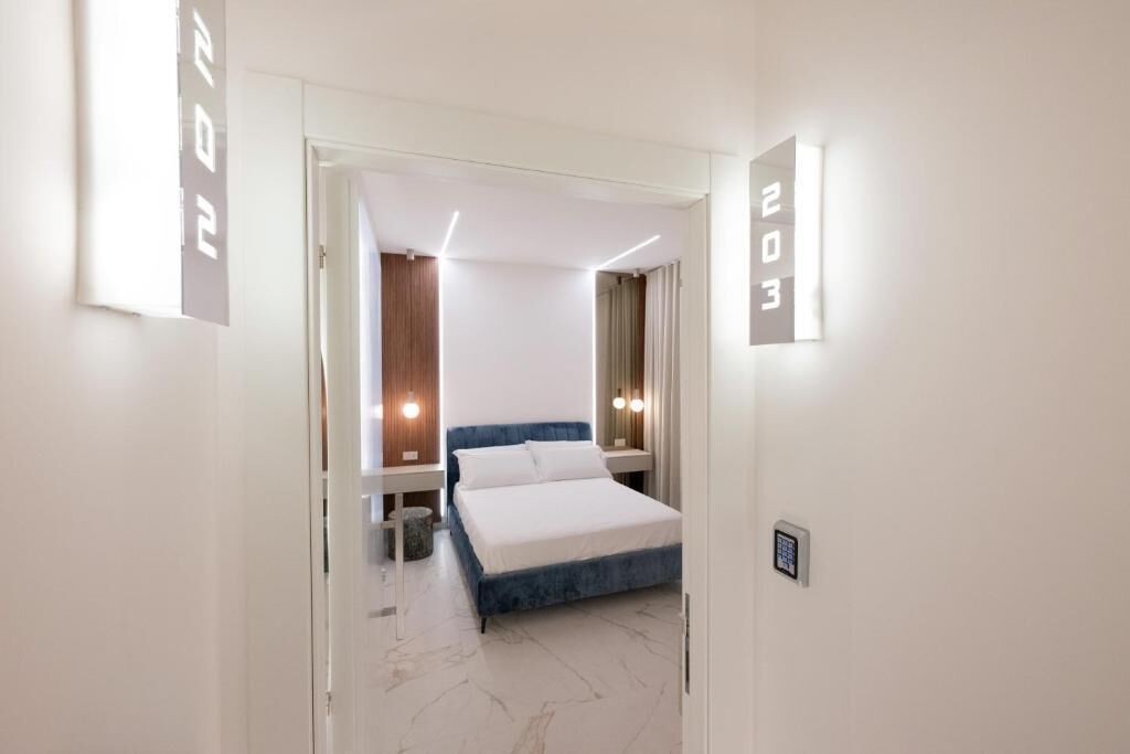 A modern hotel room with a bed, bedside tables, and a digital lock.