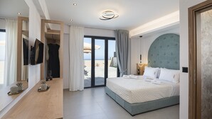 A modern hotel room with a bed, a wooden desk, a large mirror, and a view of the beach. - Villa Selene – Luxury Sea View Villa (Panormo)