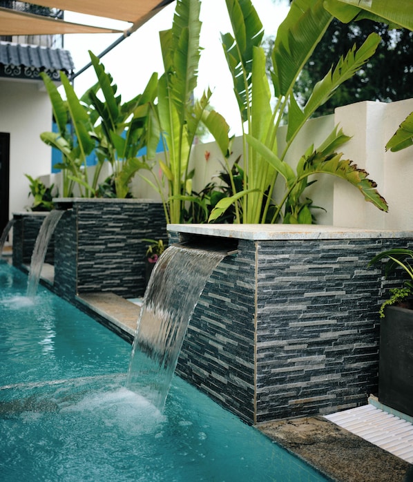 Piscina con cascada, rodeada de muros de piedra y abundante vegetación.