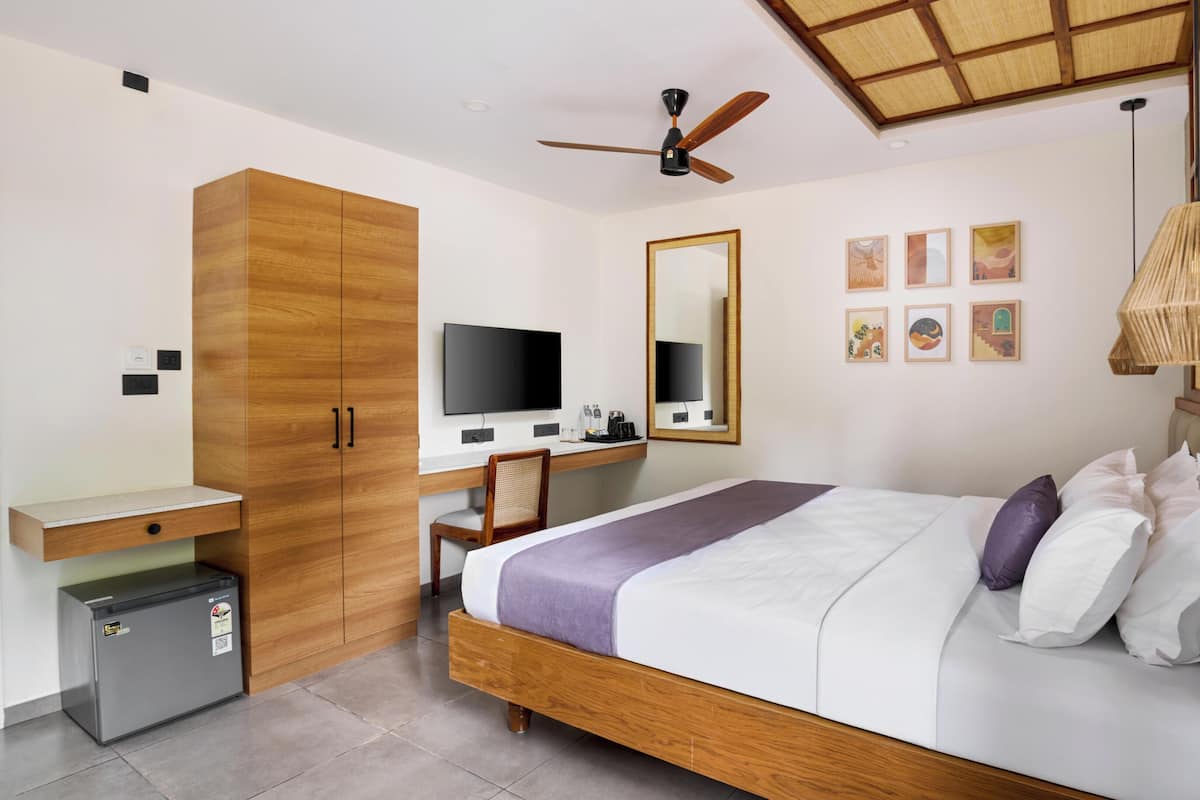 Una habitación de hotel moderna con una cama de madera, un escritorio con computadora, un ventilador de techo y un refrigerador pequeño.