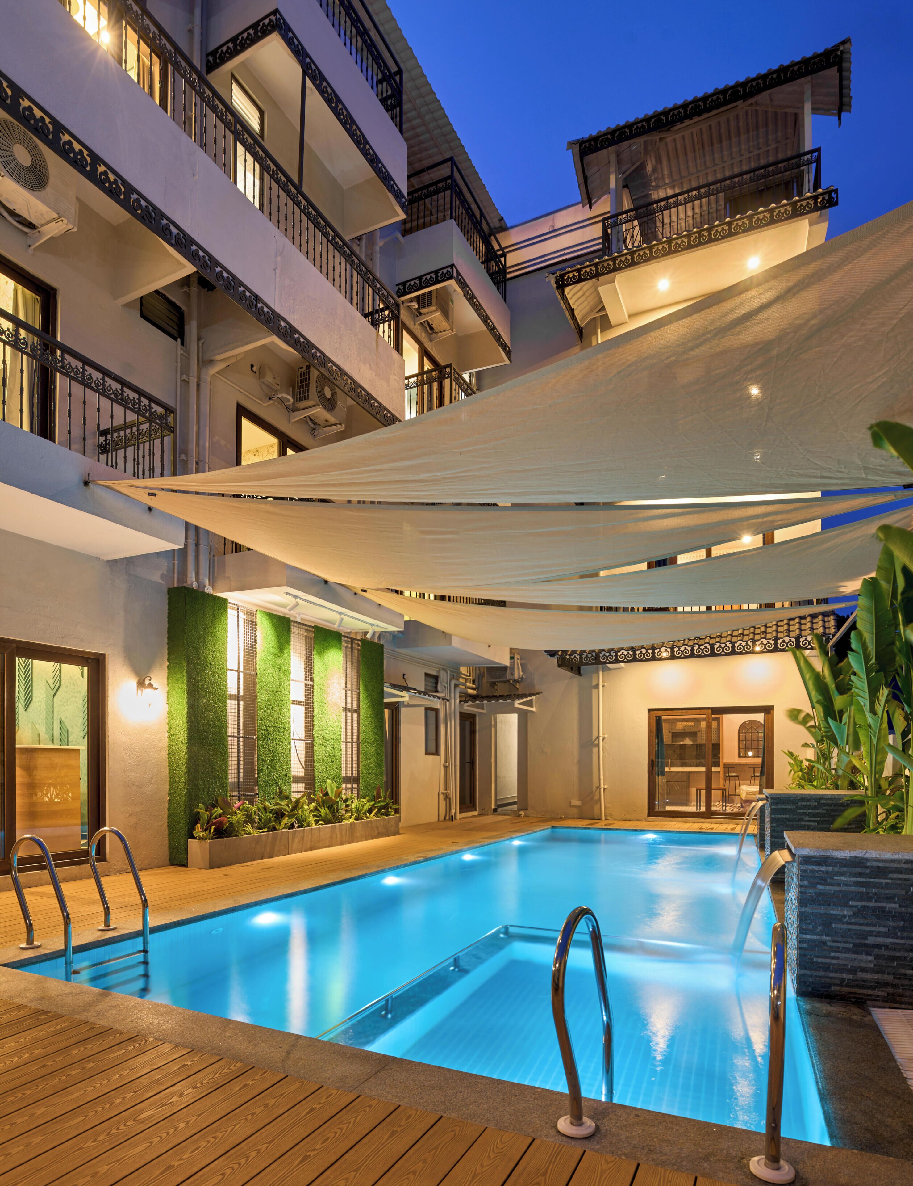 A swimming pool with a wooden deck, surrounded by a building with balconies and a covered area.