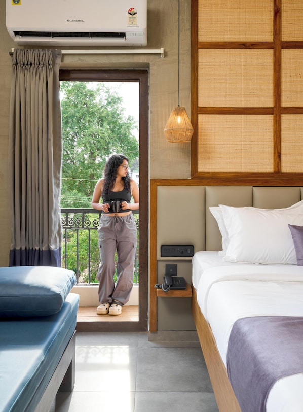 Habitación de hotel con cama, mesita de noche con teléfono, ventana con cortinas y equipo de aire acondicionado.