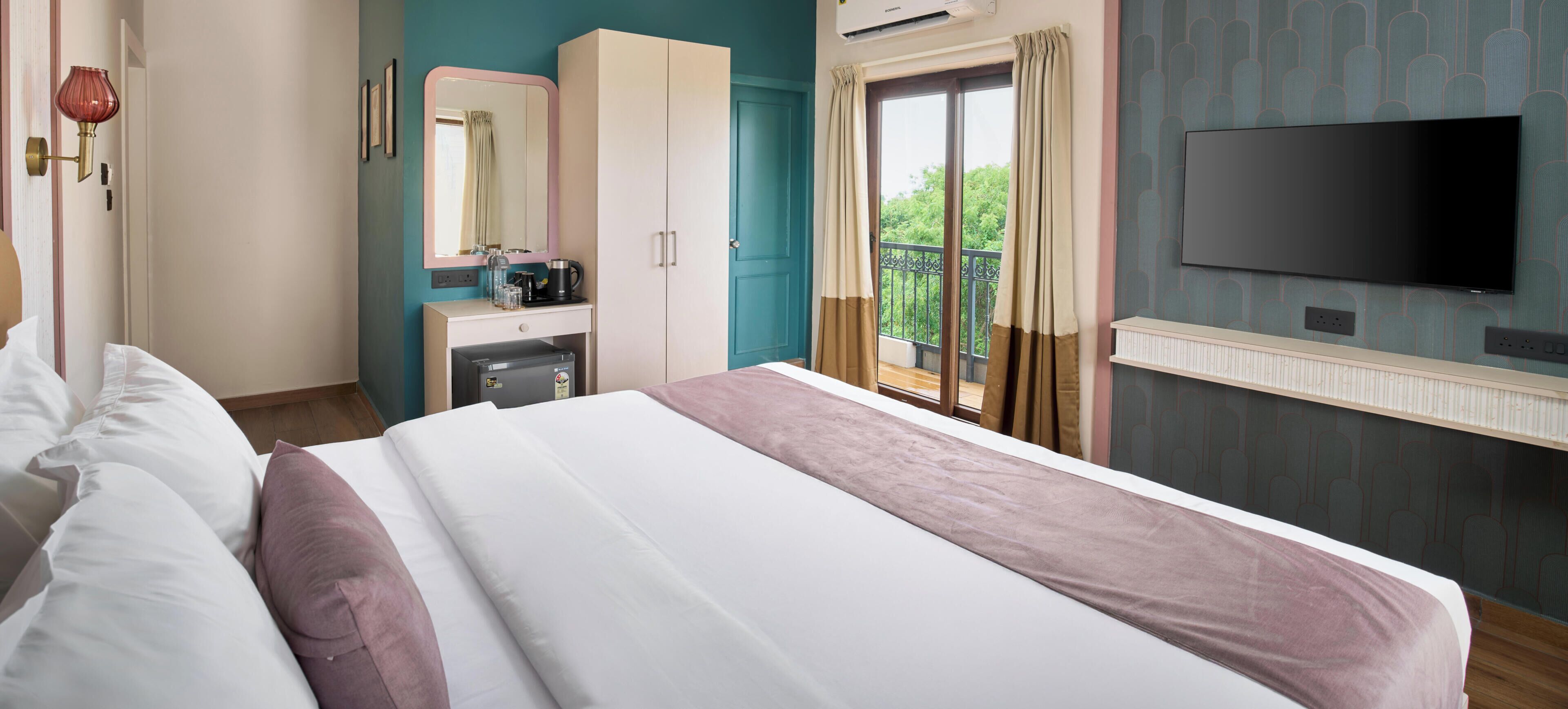 Habitación de hotel con cama, armario, escritorio con espejo, televisor y balcón con vistas.