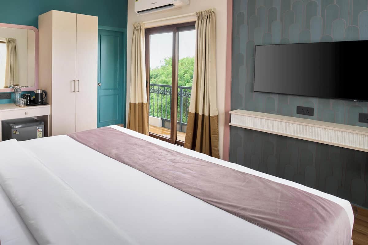 Habitación de hotel con cama, armario, escritorio con espejo, televisor y balcón con vistas.