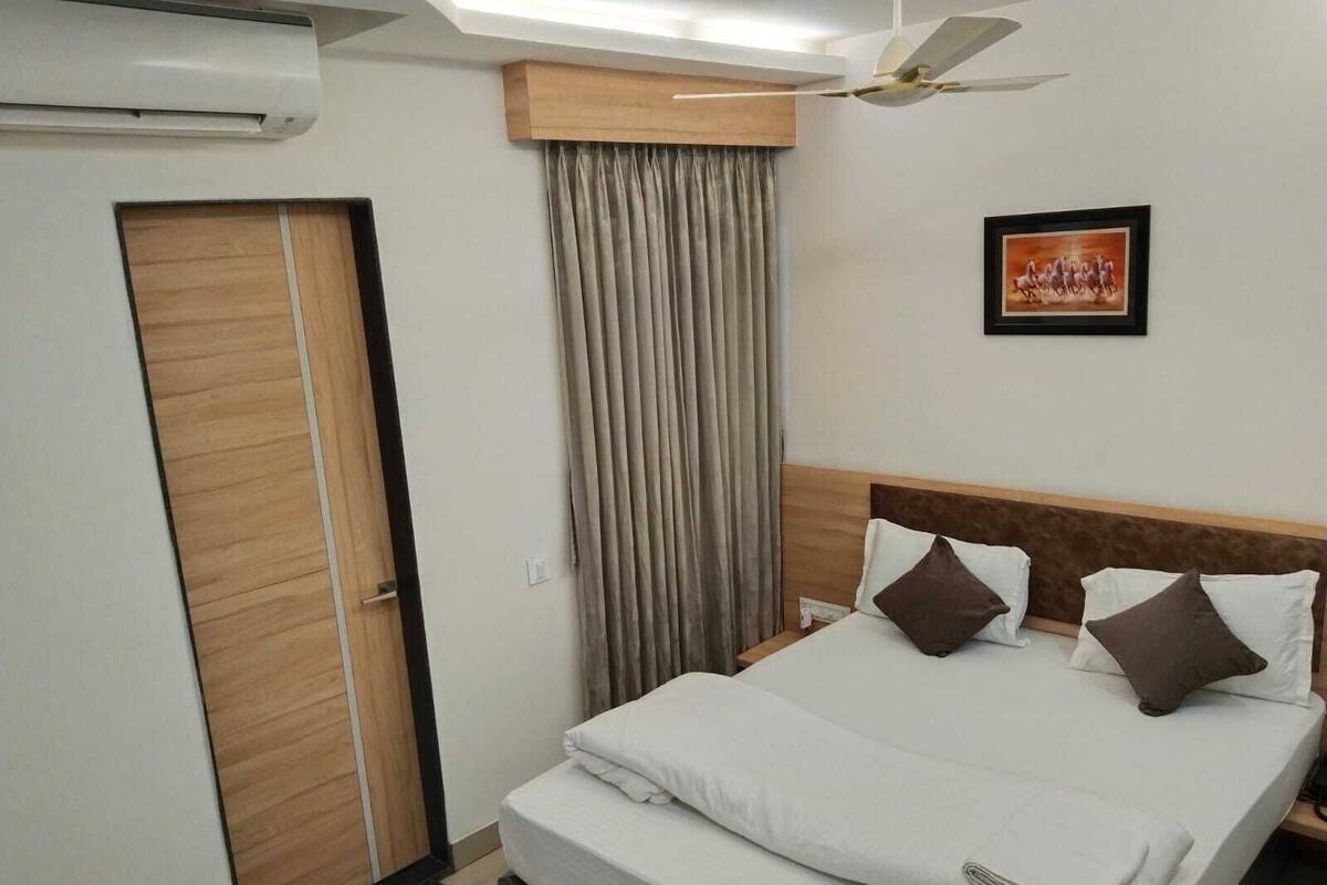 A hotel room with a bed, a ceiling fan, a painting, and a door.