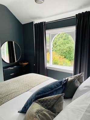 Ein Schlafzimmer mit Bett, Kommode, Spiegel und einem Fenster mit Vorhängen.