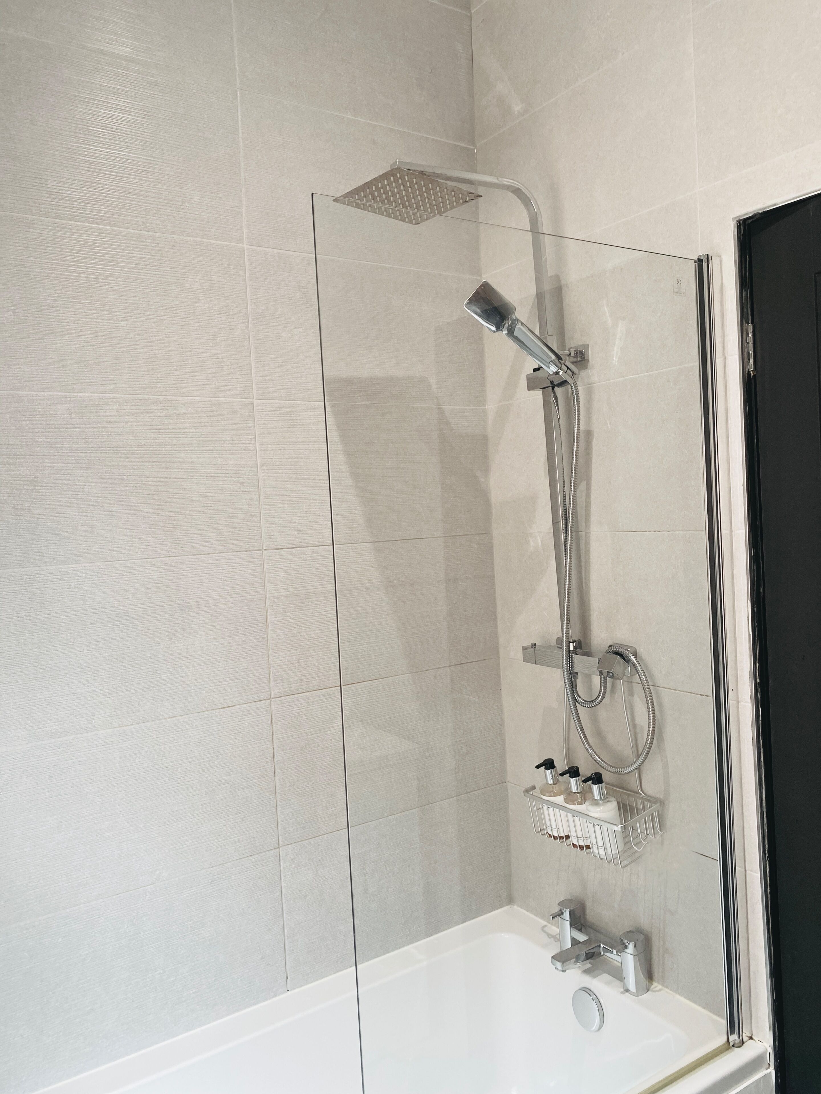 A modern bathroom with a glass-enclosed shower, a white bathtub, and a chrome showerhead.