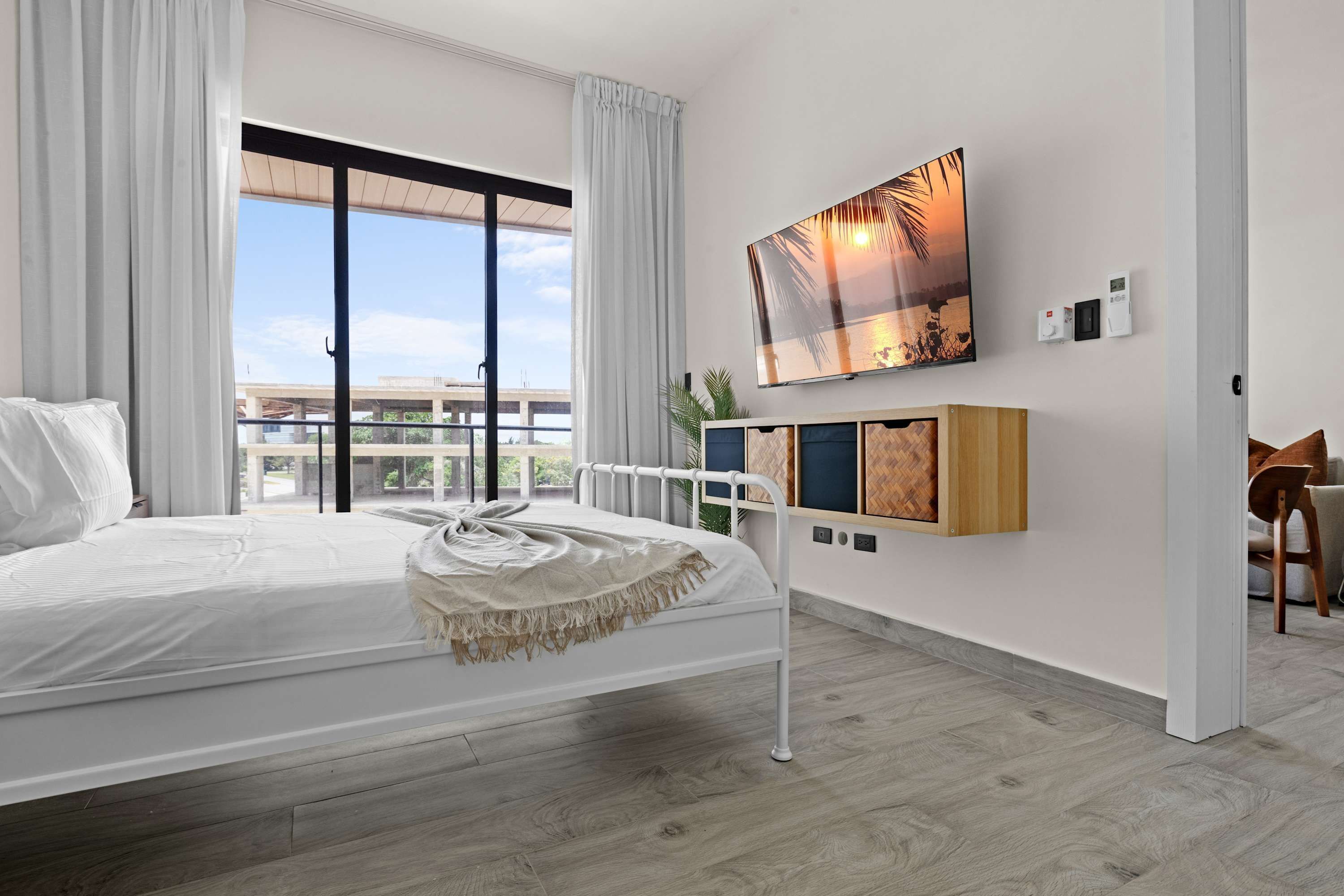 A modern hotel room with a large bed, a TV mounted on the wall, and a balcony with a view of the city.