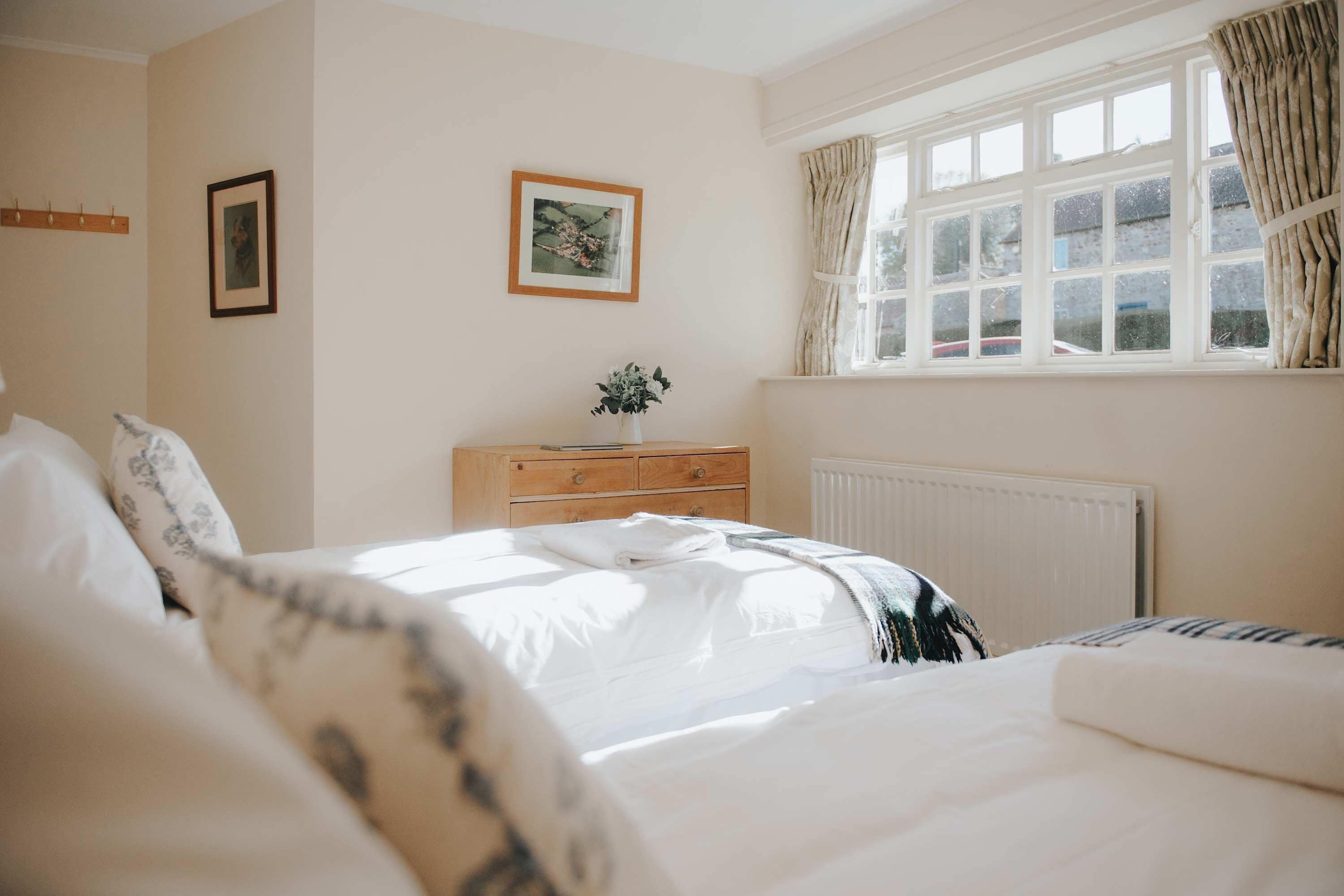 A bedroom with a bed, a nightstand, a dresser, a window with curtains, and wall-mounted pictures.