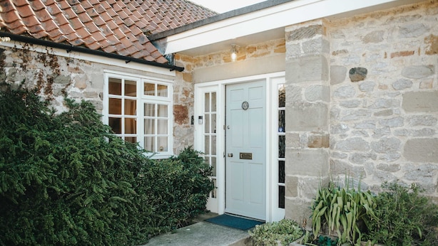 A stone house with a white door, a small porch, and a gravel pathway. - Traditional Cottage Near Richmond Yorkshire Dales (Richmond)
