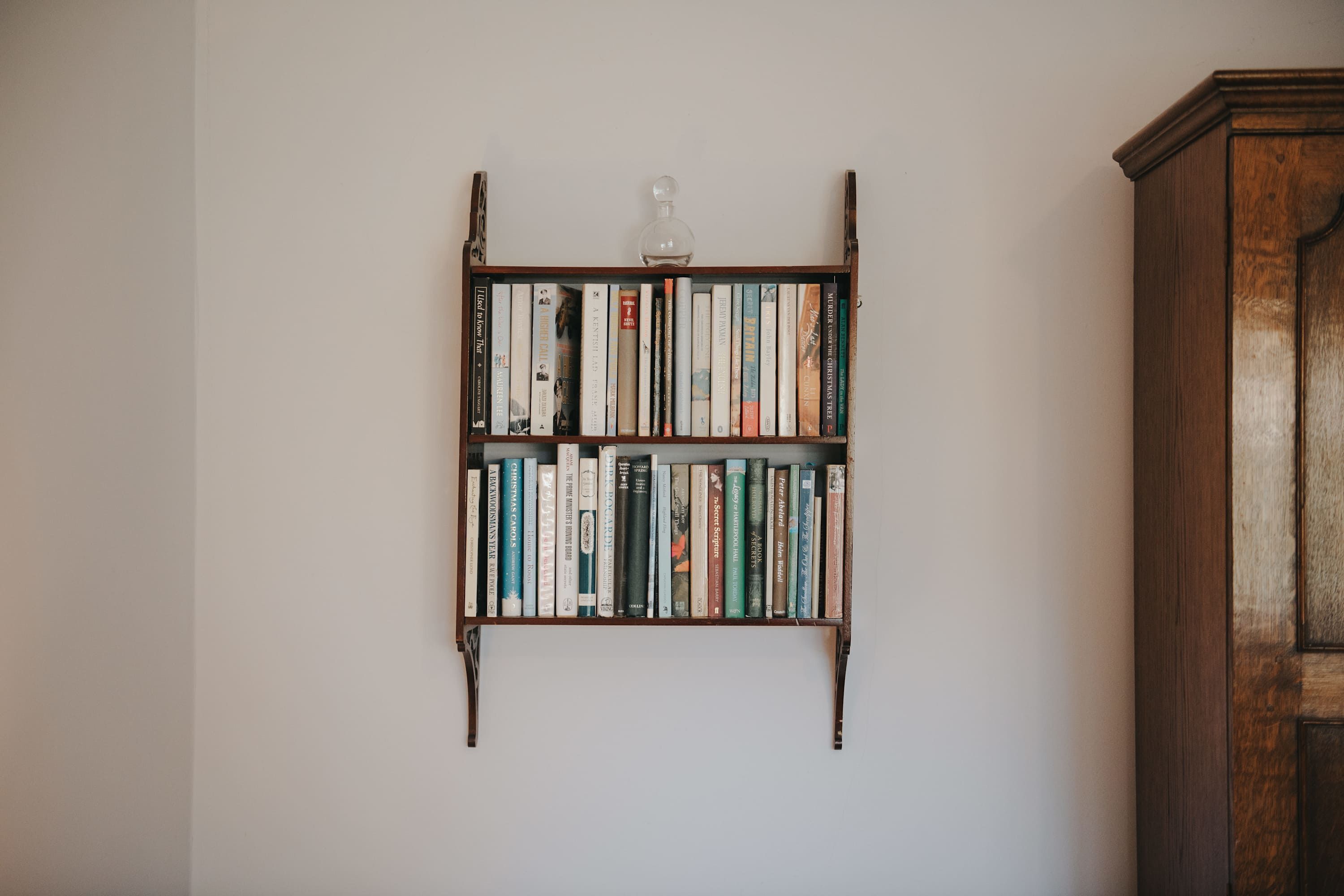 Una estantería con libros y una botella de vidrio en la pared.