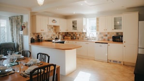 A modern kitchen with white cabinetry, a central island, and a dining area with chairs and a table set for four. - Traditional Cottage Near Richmond Yorkshire Dales (Richmond)