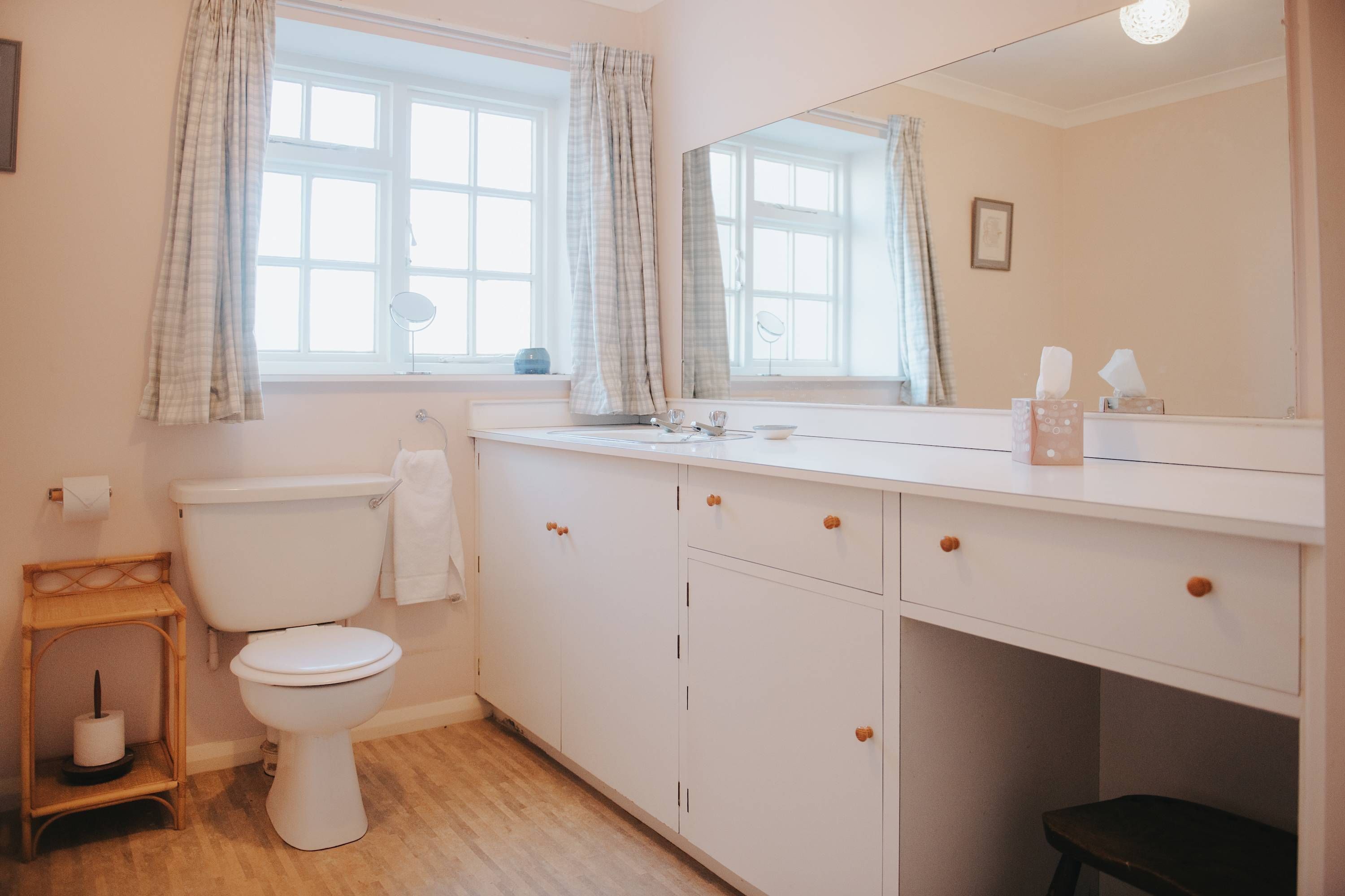 Une salle de bain avec des toilettes, un lavabo avec un miroir et une fenêtre avec des rideaux.