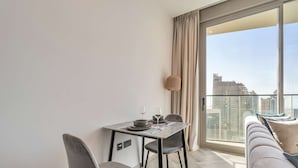 Een moderne eetruimte met een tafel, stoelen en een bank, met uitzicht op een stadsbeeld door grote ramen.