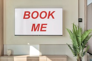 Ein an der Wand befestigter Fernseher mit dem Schriftzug 'BOOK ME' in roten Buchstaben.