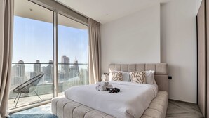 Een moderne hotelkamer met een groot bed, een stoel en uitzicht op de stad door middel van kamerhoge ramen.