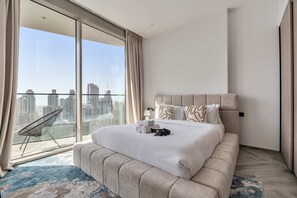 Ein modernes Hotelzimmer mit einem großen Bett, einem Sessel und Blick auf die Stadt durch raumhohe Fenster.