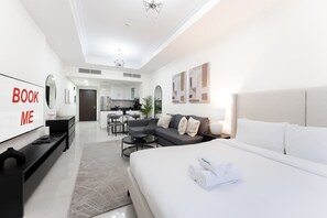 A modern hotel room with a large bed, a TV, a sofa, and a dining area in the background. - Free Housekeeping Visits During Your Stay - Stayshort - Spacious Studio Apartment With Balcony That Sleeps 4 (Dubai)