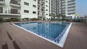 En swimmingpool på taget med liggestole, omgivet af en høj boligbygning.