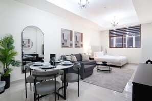 A modern living room with a dining area, a sofa, a bed, and a large window. - Free Housekeeping Visits During Your Stay - Stayshort - Spacious Studio Apartment With Balcony That Sleeps 4 (Dubai)