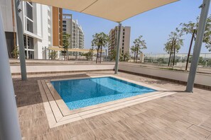 En pool på taget med fliseterrasse, omgivet af moderne bygninger og træer.