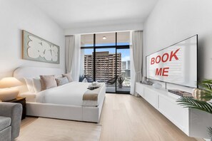 A modern bedroom with a large bed, a TV, and a view of a high-rise building. - Free Housekeeping Visits During Your Stay - Stayshort - Modern Studio That Sleeps 4 at Riviera Beachfront (Dubai)