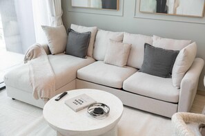 Ein modernes Wohnzimmer mit einem beigefarbenen Ecksofa, einem runden Couchtisch und einem Buch mit dem Titel 'Eat Drink Map'.
