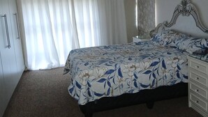 Un dormitorio con cama, ventilador de techo, ventana con cortinas, cómoda y armario.