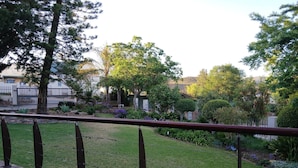 Una terraza con barandilla de metal que da a un jardín cuidado, con diversas plantas y árboles.
