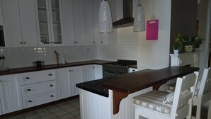 Una cocina con armarios blancos, una isla de madera, una estufa a gas, lámparas colgantes y una planta en maceta.