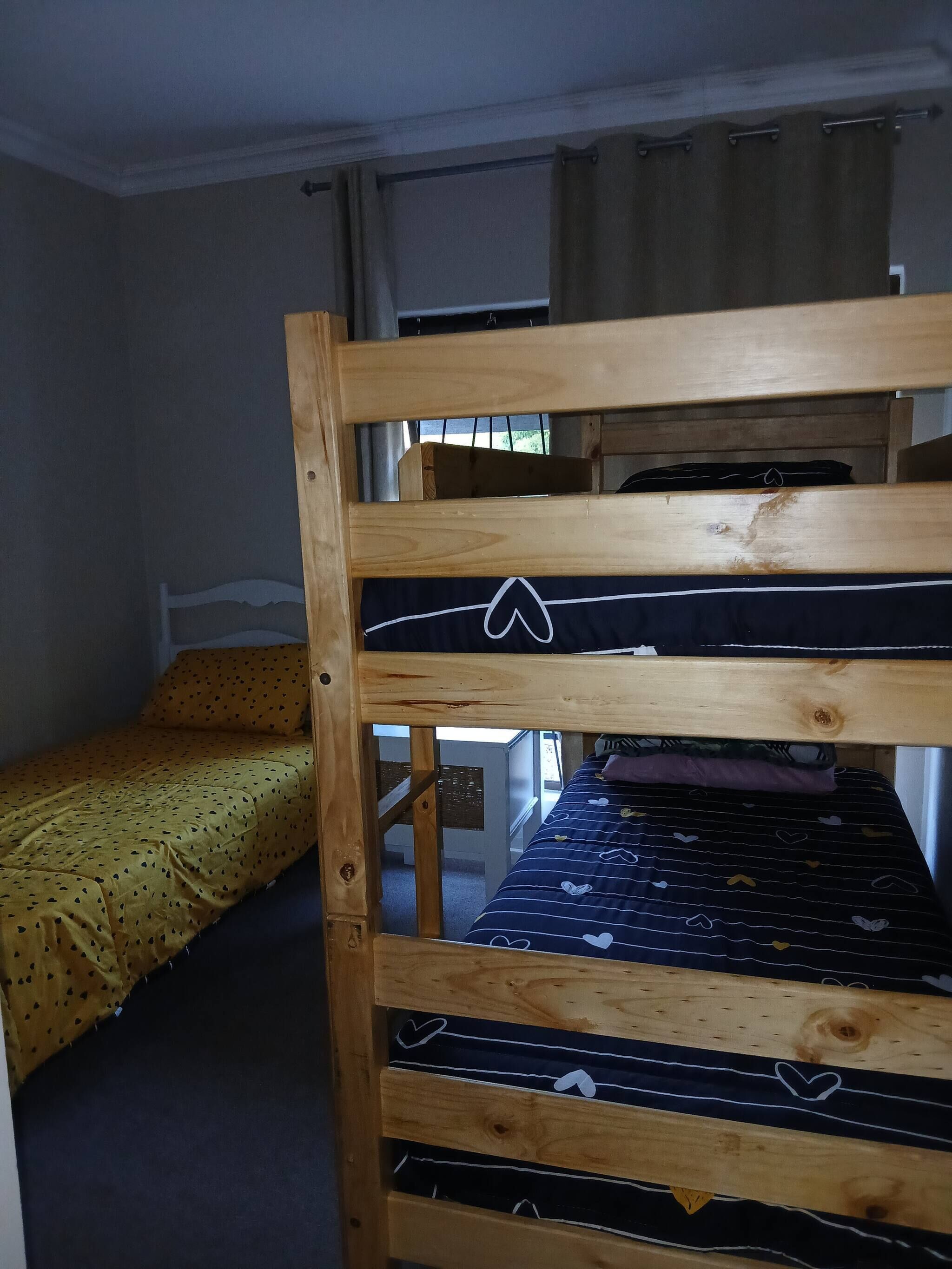 A bunk bed with a wooden frame, a lower bed with a yellow bedspread, and a window with curtains.