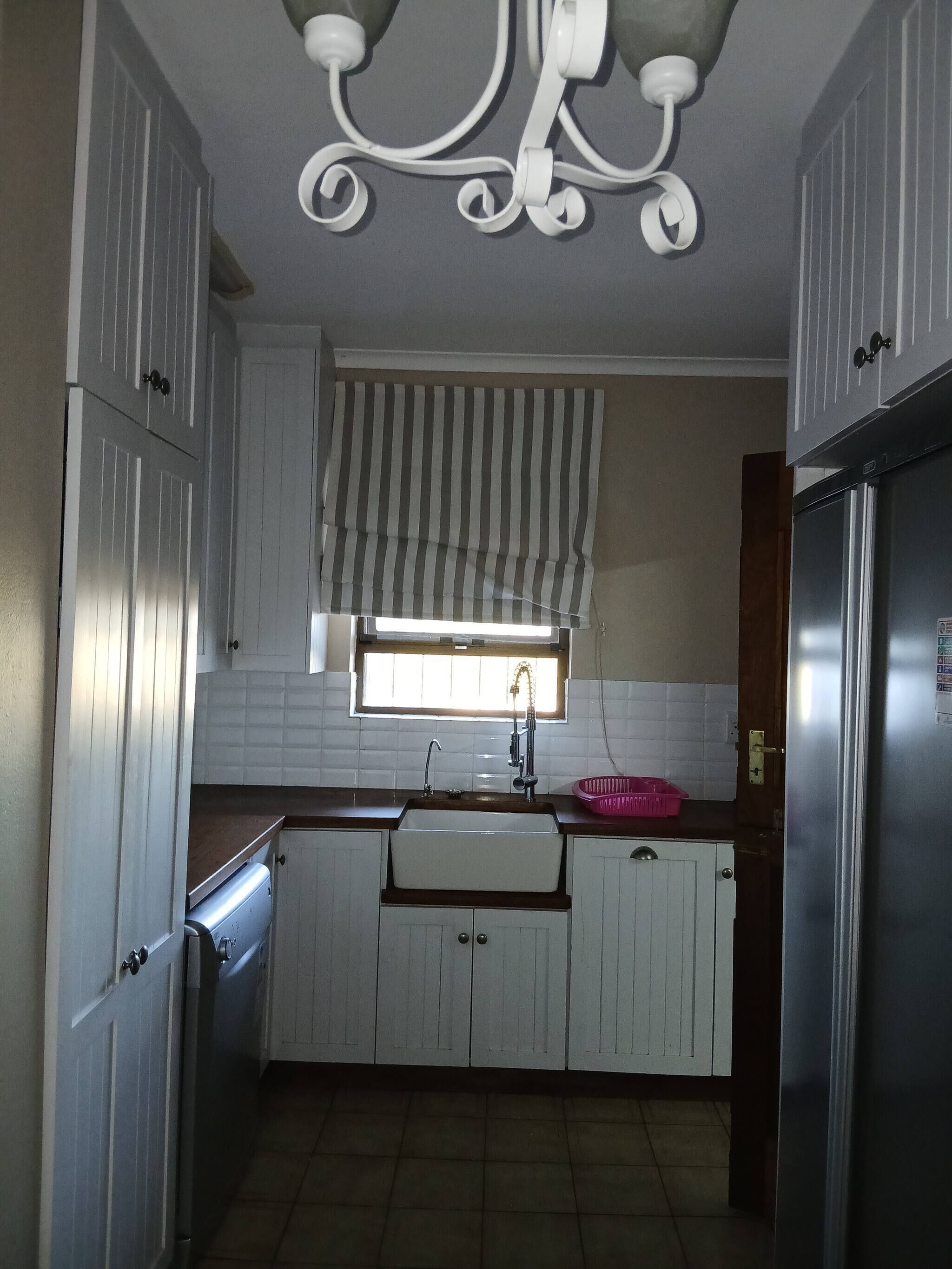 A kitchen with white cabinets, a stainless steel refrigerator, a window with striped blinds, and a sink.