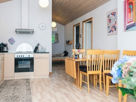 Cocina compacta con estufa, horno y radio, un comedor con sillas de madera, y una cama al fondo.