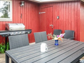 An outdoor patio with a grill, wicker chairs, a table, and a vase of flowers. - 4 Star Holiday Home in Juelsminde (Juelsminde)