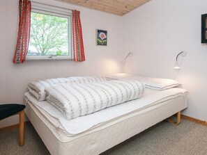 A neatly made bed with a white and patterned duvet, a single bedside lamp, and a window with curtains. - 4 Star Holiday Home in Juelsminde (Juelsminde)