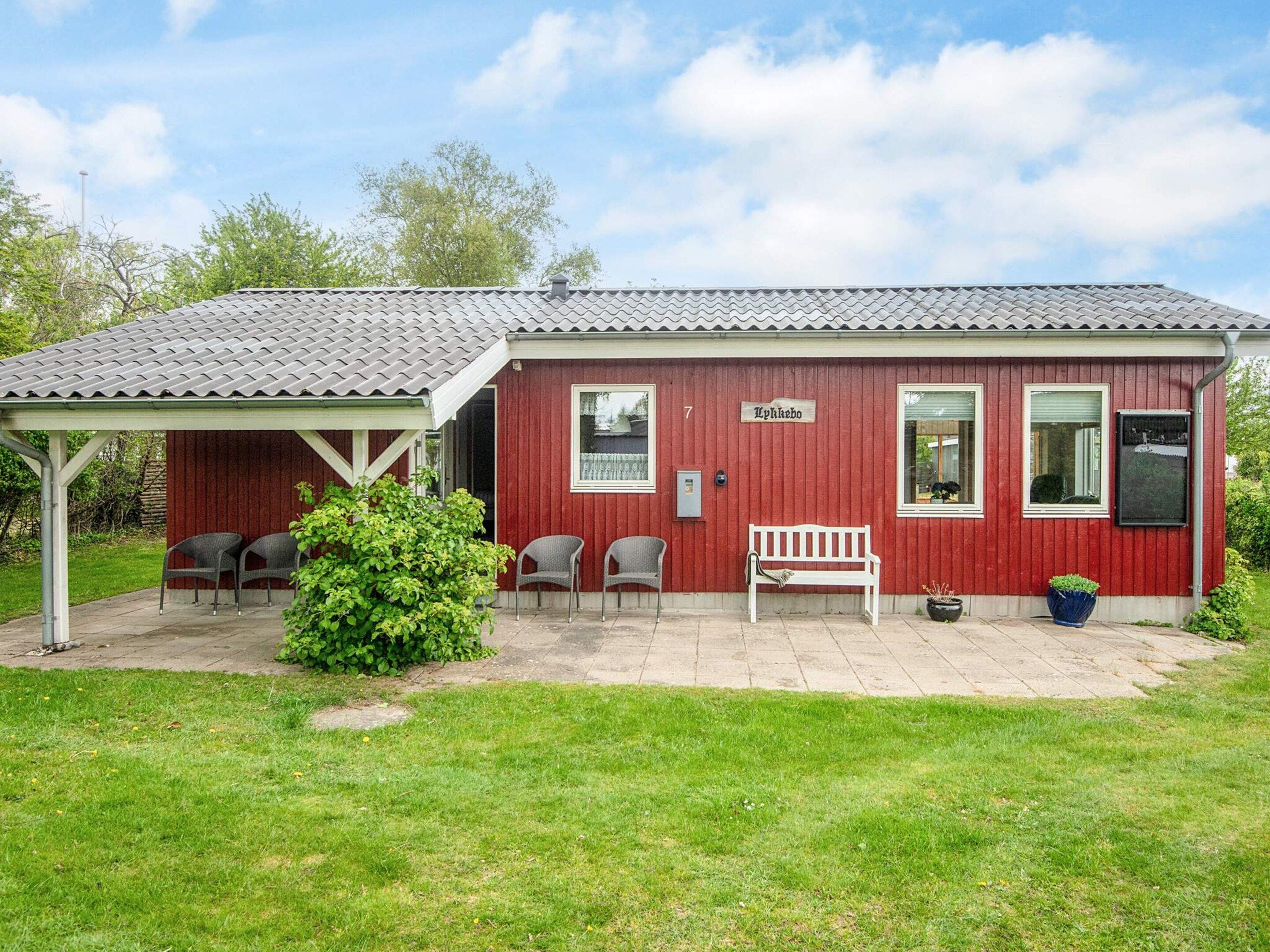 A red building with a covered patio, a bench, and two chairs.