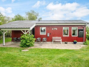 A red building with a covered patio, a bench, and two chairs. - 4 Star Holiday Home in Juelsminde (Juelsminde)