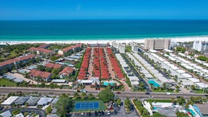 Luchtbeeld van een kusthotel met meerdere gebouwen, een strand en een helderblauwe lucht.