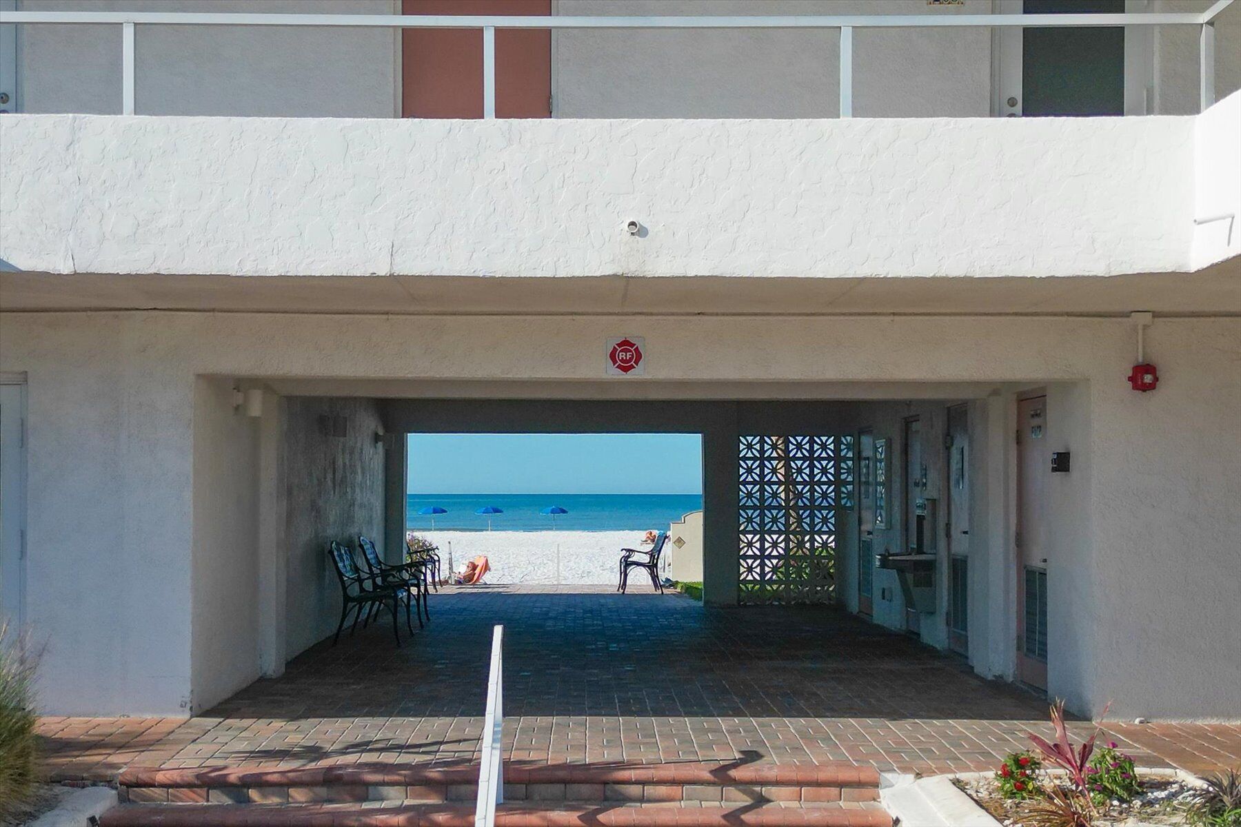 A building entrance with a view of the beach, outdoor seating, and a covered patio area.