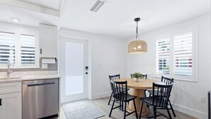 Een moderne keuken met een vaatwasser, een eettafel met stoelen, een hangende lamp en een deur met raam.