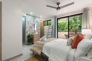 A bedroom with a bed, a ceiling fan, a window with a view of greenery, a bedside table, and a nightstand. - Luxury Villa with Private Pool, Jungle Views, fully staffed!  Minutes from the Beach (Tamarindo)