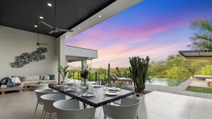Zona pranzo moderna con vista su un paesaggio lussureggiante e un tramonto.
