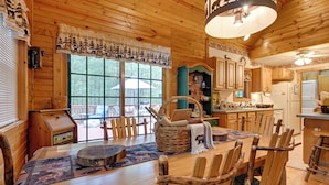 A wooden cabin interior with a dining table, chairs, a basket, and a refrigerator.