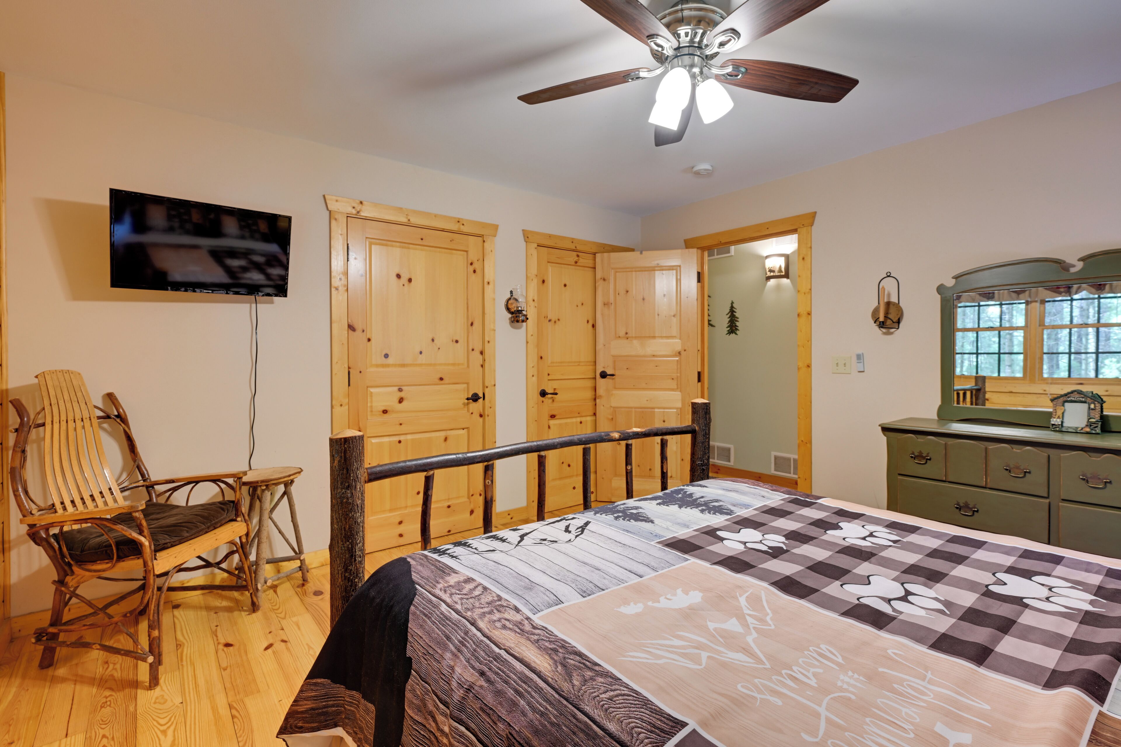 Un dormitorio con cama, armario de madera, una silla, televisor y ventilador de techo.