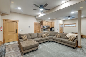 A living room with a sectional sofa, wooden cabinets, a ceiling fan, and a kitchen area. - 3 Units at Getaway Lodges! West Yellowstone Base (Island Park)