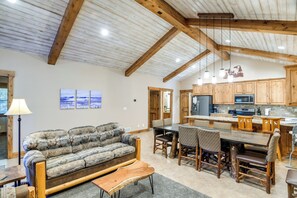 Amplia sala de estar con un sofá grande, una mesa de centro de madera y un comedor con una mesa larga y sillas. La cocina cuenta con muebles de madera y una isla central.