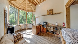 A spacious room with a wooden ceiling, large windows, a kitchenette, and a bed. - Whidbey Island Tiny Home Near Trails & Beaches! (Oak Harbor)