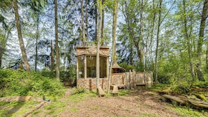 A wooden cabin in a forest with a glass door, surrounded by trees and a wooden deck. - Whidbey Island Tiny Home Near Trails & Beaches! (Oak Harbor)